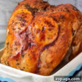 A deliciously roasted turkey crown with fragrant herbs graces a white baking dish, perfectly complemented by the rustic charm of a brick backdrop.