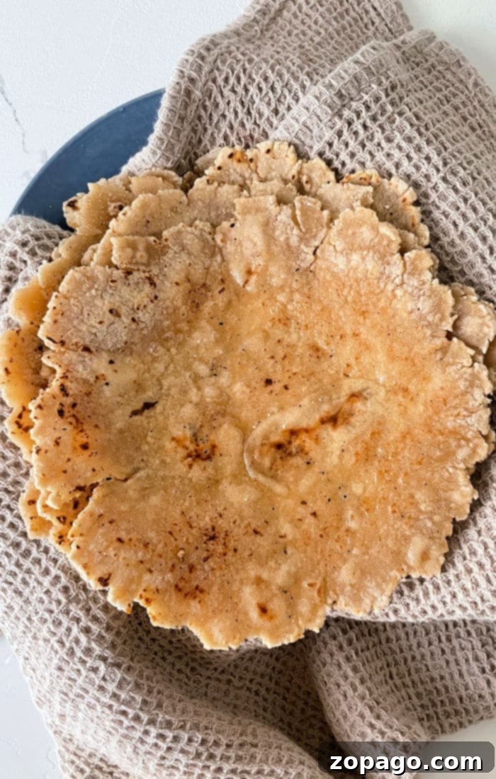A stack of homemade roti flatbreads on a textured cloth, illustrating how to make roti perfectly.