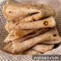 A stack of folded flatbreads, perfect for a gluten-free roti recipe, rests elegantly on a textured, light brown cloth.