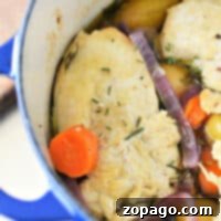 Dutch Oven Chicken Breast 5 A blue Dutch oven brimming with tender chicken breast, carrots, potatoes, and red onions in a savory broth, all garnished with fragrant rosemary.