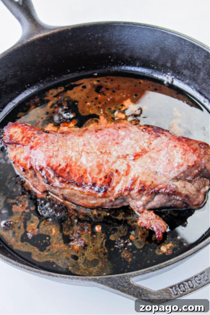 Cast Iron Seared Flank Steak 4 A juicy flank steak sizzles in a cast iron skillet against a pristine white background.