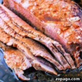 Sliced roasted flank steak nestled in a cast iron pan with flavorful juices.