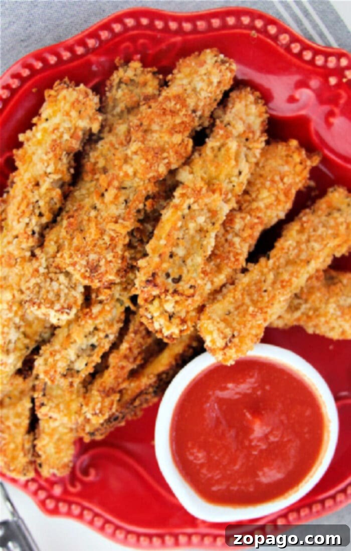 Plate of crispy breaded eggplant fries with a side of vibrant red dipping sauce, ready to be enjoyed.