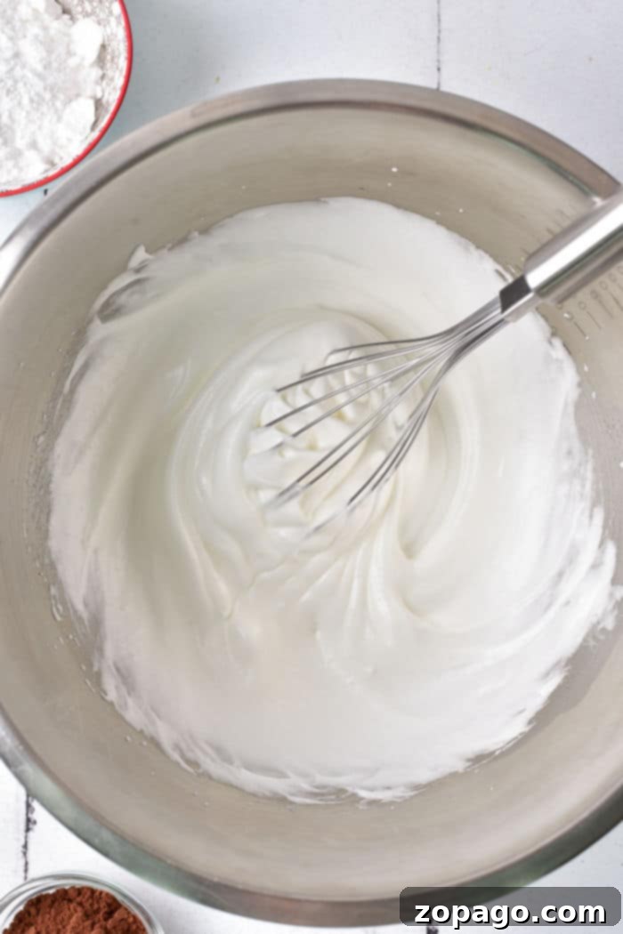 Zesty Lemon Meringue Strawberry Shortcake 3 Close-up of a whisk in a mixing bowl, lifting fluffy, whipped egg whites, perfectly poised for crafting an exquisite meringue.