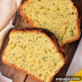 Two slices of zucchini lemon poppy seed bread rest on a wooden board with a lemon wedge nearby.