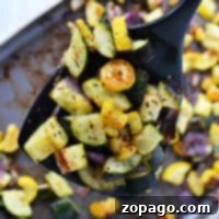 A spoonful of perfectly roasted zucchini and squash, accompanied by tender onions, adorns the baking tray.