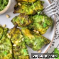 Air Fryer Pesto Chicken pieces are perfectly grilled and coated in green pesto sauce, served on a plate garnished with fresh greens and pine nuts.