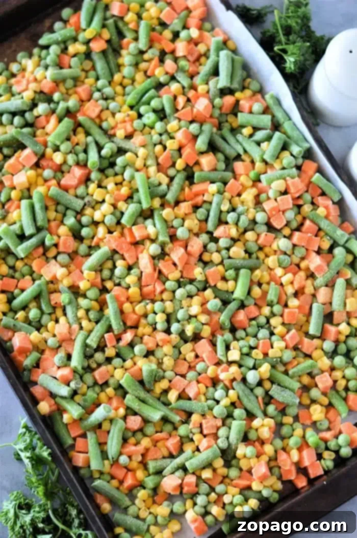 Crispy Roasted Frozen Vegetables 3 A baking sheet brimming with roasting frozen vegetables, including green beans, corn, peas, and diced carrots. Fresh parsley peeks out in the background.