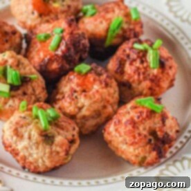 A white decorative plate features several golden brown air fryer chicken meatballs, garnished with chopped green onions. The perfectly cooked meatballs are arranged closely together for a delicious presentation.