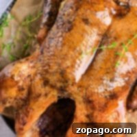 A succulent roast duck with golden skin, garnished with fresh thyme, rests enticingly on a parchment-lined plate.