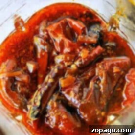 Red chili pickle soaked in oil and spices, with visible whole red chilies and seeds in a glass jar—perfect as a fiery Birria Tacos Sauce or zesty condiment.