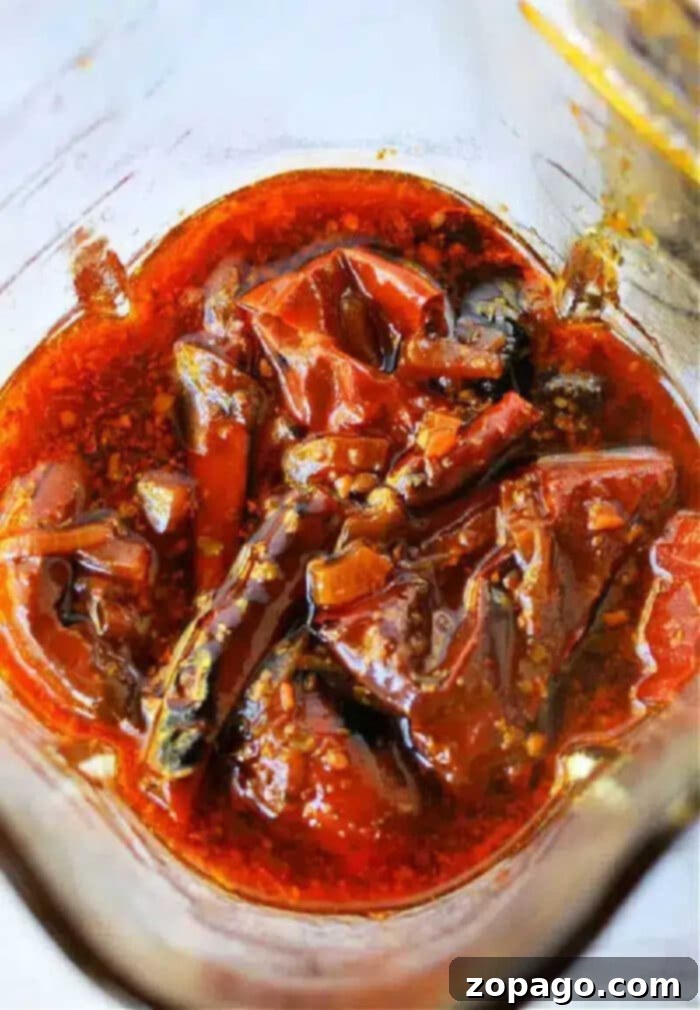 Birria Taco Sauce 9 Red chili pickle soaked in oil and spices, with visible whole red chilies and seeds in a glass jar—perfect as a fiery Birria Tacos Sauce or zesty condiment.