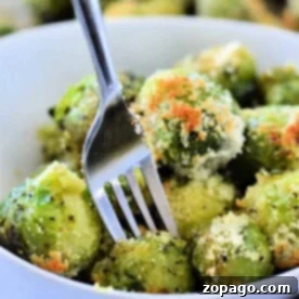 A bowl of microwaved Brussels sprouts with Parmesan cheese, how to microwave Brussels sprouts to perfection, all flawlessly pierced by a fork.