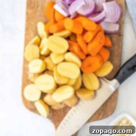 Chopped potatoes, carrots, and red onions on a wooden cutting board await a knife's touch; spices in small bowls nearby enhance the flavor of steaming vegetables in a microwave.