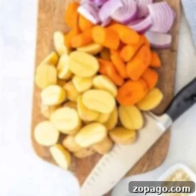 Chopped potatoes, carrots, and red onions on a wooden cutting board await a knife's touch; spices in small bowls nearby enhance the flavor of steaming vegetables in a microwave.