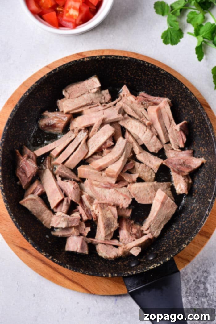Cooking Tender Beef Tongue 5 Sliced cooked tongue in a frying pan on a wooden board, next to cut tomatoes and cilantro. For those interested in expanding their culinary skills, learning how to cook cow tongue can offer a rich and delectable addition to your kitchen repertoire.