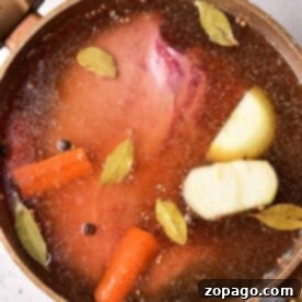A pot with simmering broth, raw cow tongue, carrots, onion, bay leaves, and peppercorns creates the perfect medley for a sumptuous meal.