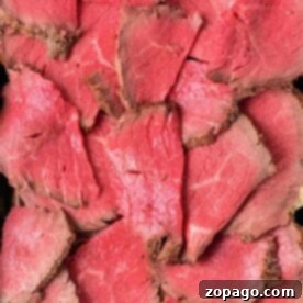 Slices of rare roast beef layered in a metal tray, showing a pink center and browned edges—perfect for anyone wanting to learn How to Cook Melt in the Mouth Roast Beef.