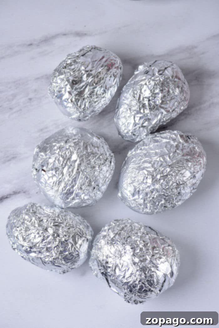 Perfectly Roasted Red Potatoes 5 Six baked red potatoes are wrapped in crumpled aluminum foil and placed on a white marble surface.