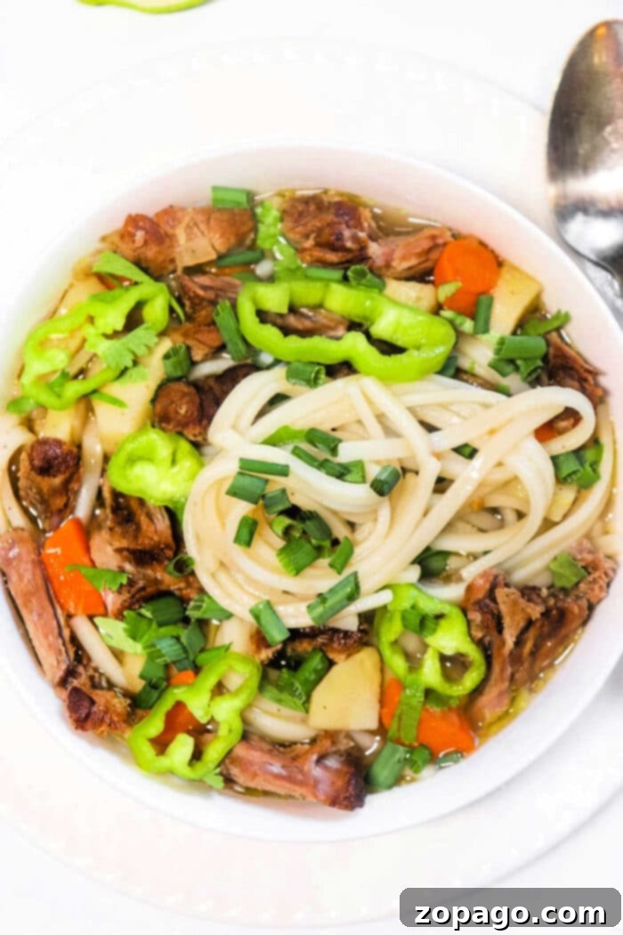 Rich Oxtail Pho 2 A bowl of oxtail pho brimming with vegetables, beef, and chives, garnished with green peppers.