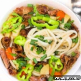A bowl of oxtail pho brimming with vegetables, beef, and chives, garnished with green peppers.