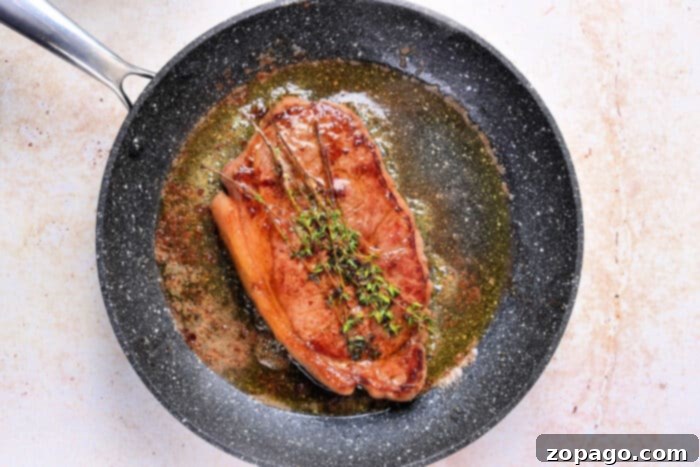Frozen Steak Sous Vide Perfection 5 A perfectly cooked Sous Vide Frozen Steak with herbs and sauce in a black frying pan on a light surface.