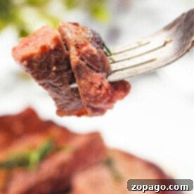 A fork holds juicy, sous vide-cooked steak pieces, perfectly seared from their frozen state amidst a softly blurred background.
