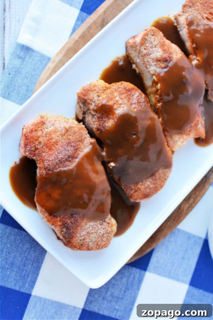 Mastering Frozen Pork Chops 6 Four succulent, seasoned pork chops, cooked from frozen, generously topped with rich brown gravy and elegantly arranged on a rectangular white plate, ready to be enjoyed.