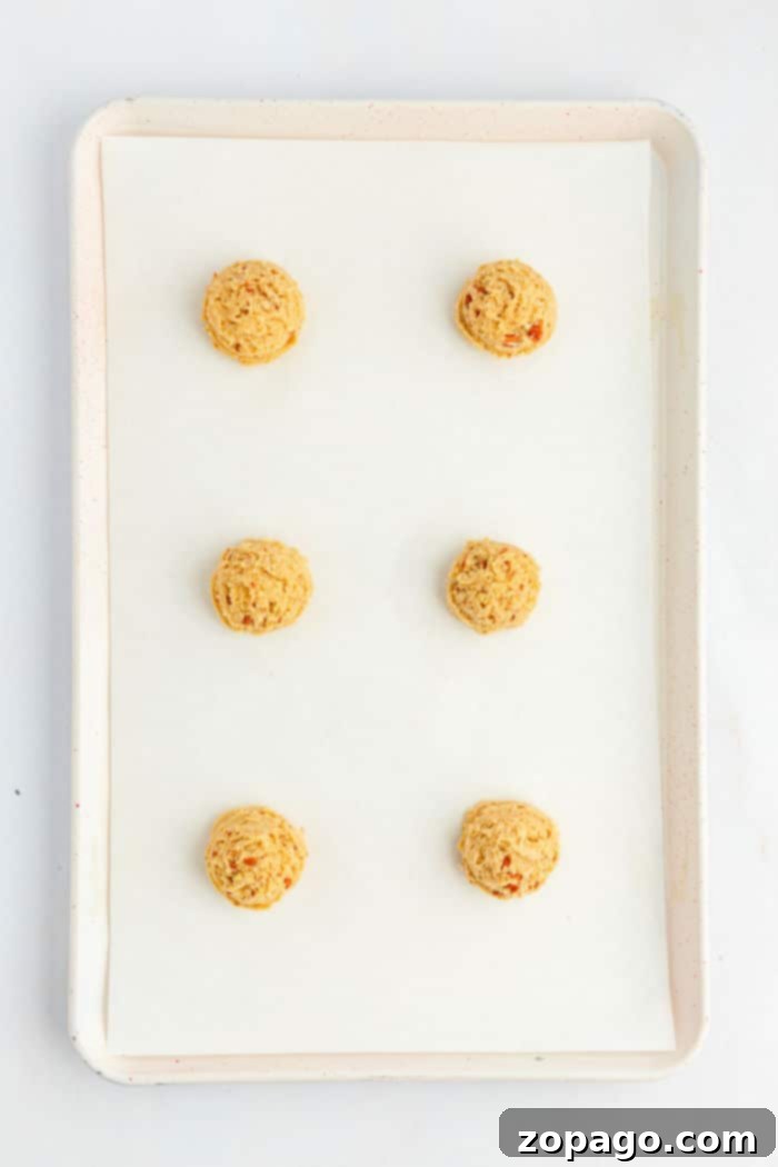 A white baking tray lined with parchment paper holds six evenly spaced raw Bear Paw Cookies dough balls arranged in two columns and three rows. The tray is shown from above against a white background.