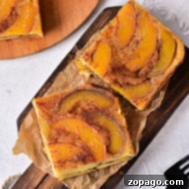 Two slices of delicious peaches cake rest on a wooden board with parchment paper, waiting to be savored, next to a gleaming fork.