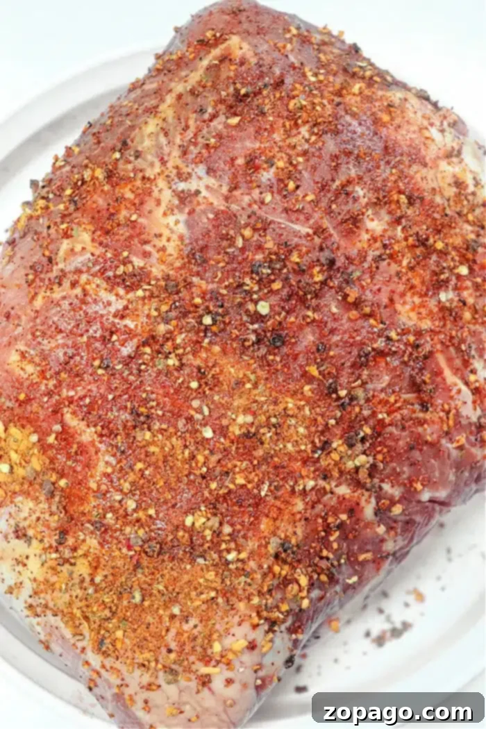 Slow-Smoked Pork 3 A raw smoked pork roast sits on a white plate, enveloped in a generous blend of red pepper flakes, ground pepper, and other fragrant herbs. The meat eagerly awaits its turn to be cooked or marinated to perfection.