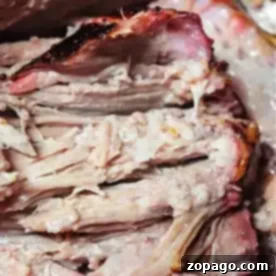 Slow-Smoked Pork 6 Close-up of sliced smoked pork roast showcasing tender, juicy meat and a reddish-brown crust. The texture appears soft and well-cooked, with visible layers and some charred edges. A fork is partially visible in the background.