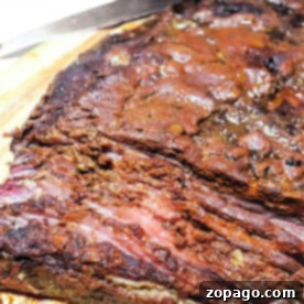 Close-up of a sliced, juicy brisket flat on a wooden cutting board with a knife nearby, showcasing the perfect blend of smoked flavor.
