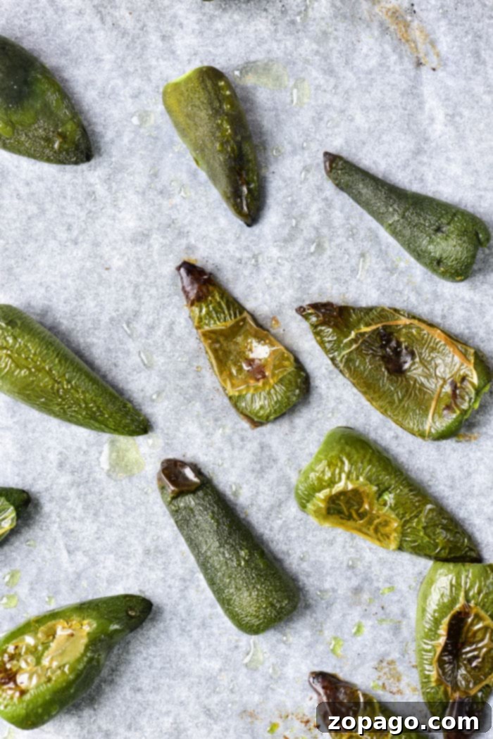 Oven-Roasted Jalapeños 5 Freshly roasted jalapenos cooling on parchment paper on a baking sheet, ready for peeling.