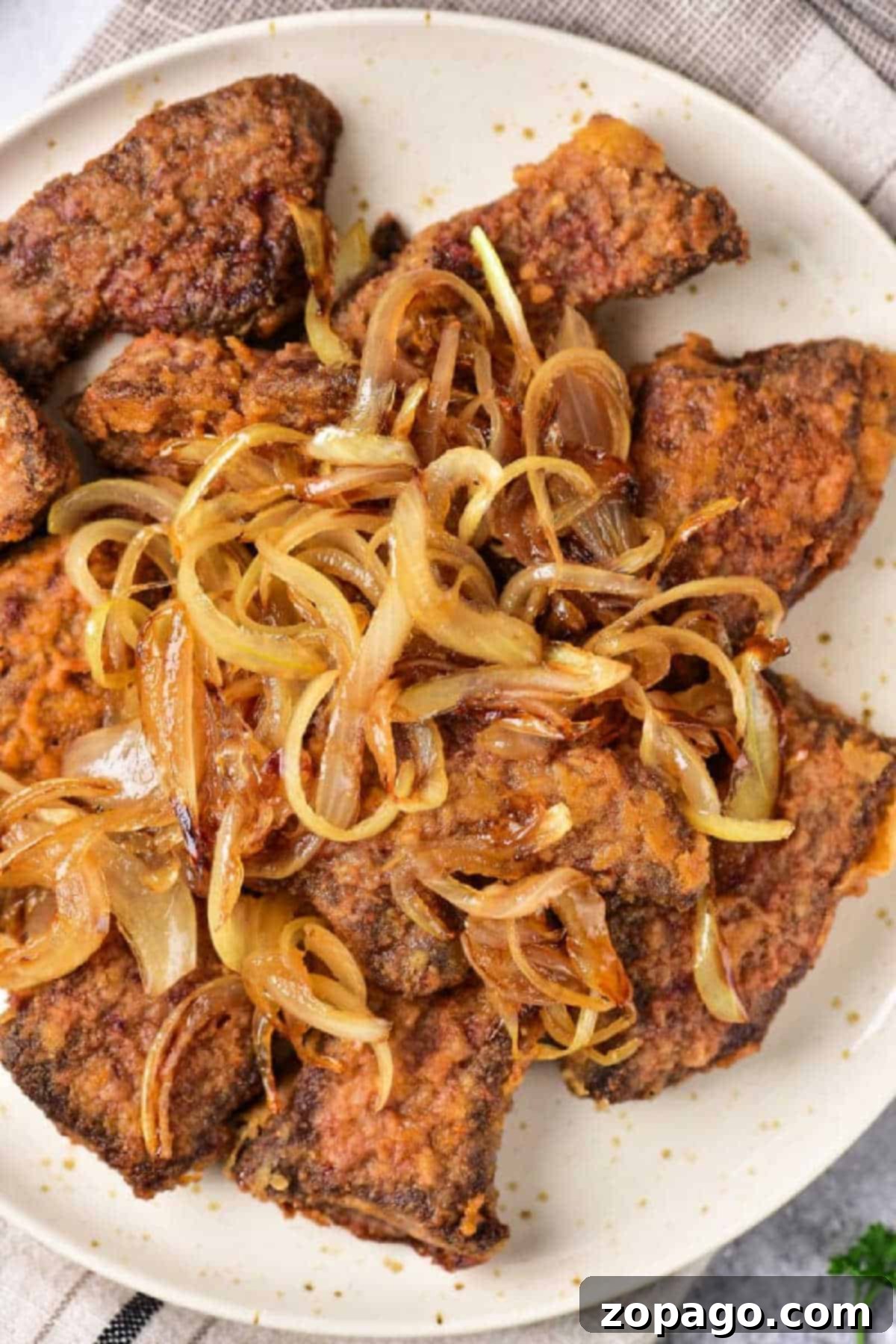 Mastering Beef Heart Cooking 2 Fried beef heart pieces topped with caramelized onions on a white plate—a classic dish for those learning organ meats, just like when discovering how to cook beef heart.