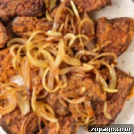 Fried beef liver pieces topped with caramelized onions on a white plate—a classic dish for those learning organ meats, just like when discovering how to cook beef heart.