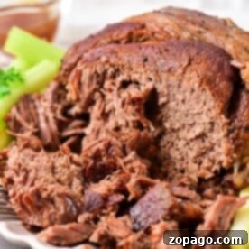 Close-up of tender beef roast shoulder shredded on a plate, adorned with a crisp garnish of celery and parsley.
