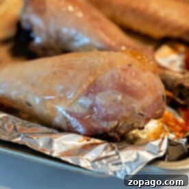 Close-up of a baked turkey leg resting on a piece of aluminum foil on a baking tray. The golden-brown exterior showcases the perfectly roasted appeal of baked turkey legs.