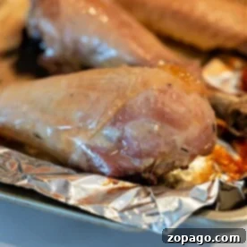 Golden Roasted Turkey Drumsticks 7 Close-up of a baked turkey leg resting on a piece of aluminum foil on a baking tray. The golden-brown exterior showcases the perfectly roasted appeal of baked turkey legs.