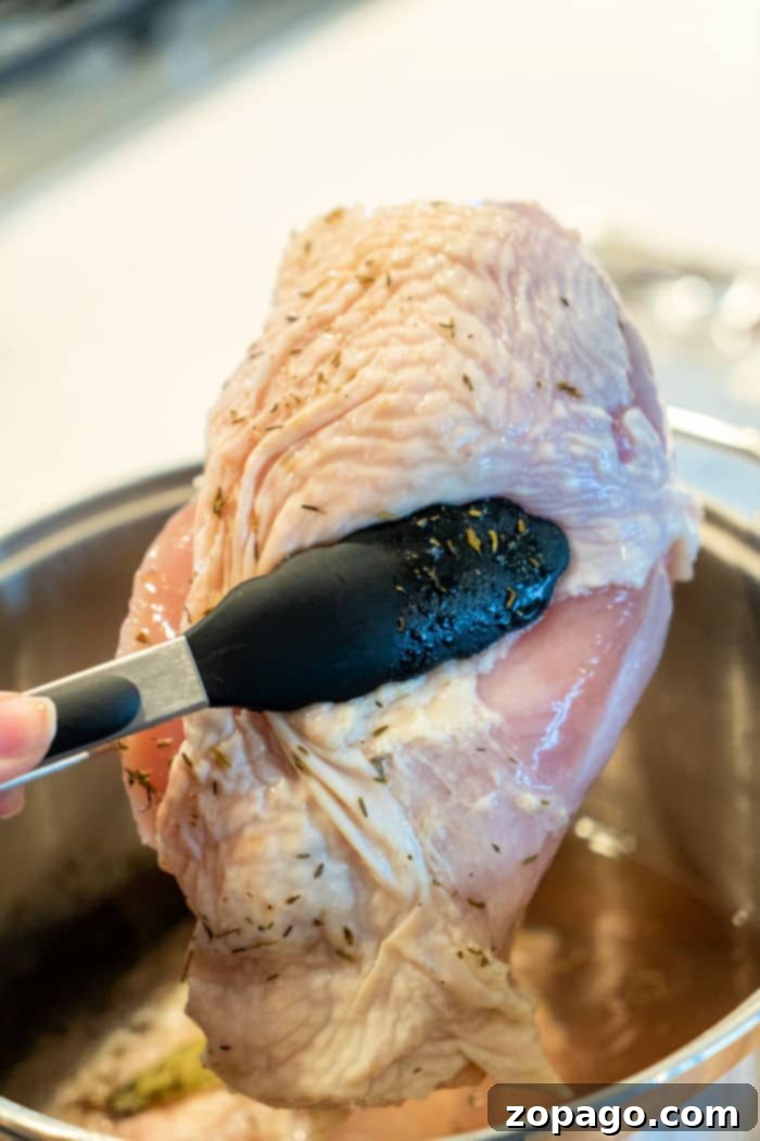 Perfect Butterball Turkey Breast Every Time 3 A close-up view of a brined turkey breast being carefully lifted from a pot with black tongs, illustrating the preparation stage for a juicy oven-roasted turkey.