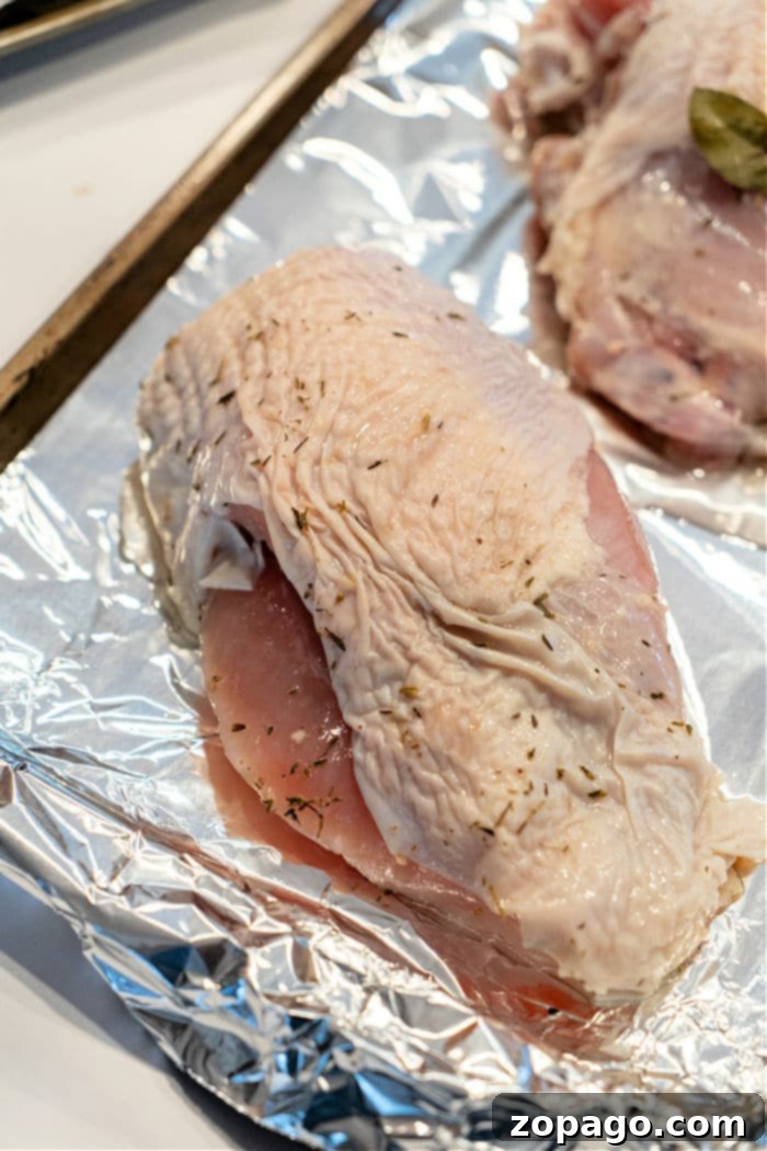 Perfectly Roasted Butterball Turkey Breast 4 Raw, seasoned turkey breast pieces, glistening with spices and olive oil, are arranged on a foil-lined baking sheet, prepared for roasting in the oven. This stage showcases the readiness for cooking a Butterball turkey breast to achieve tender, flavorful results.