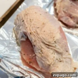 Raw turkey breast pieces seasoned with herbs on a foil-lined baking sheet, ready for roasting to a golden-brown crisp.