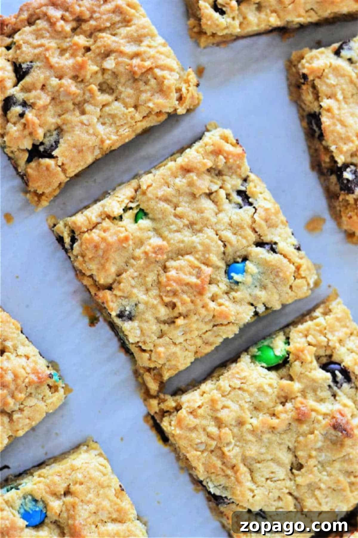 Sheet Pan Cake Mix Cookies 2 Golden cookie bars from cake mix studded with chocolate chips and colorful candy pieces, cut into squares on parchment paper, ready to be served.