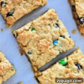 Golden cookie bars from cake mix studded with chocolate chips and colorful candy pieces, cut into squares on parchment paper.