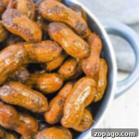 A bowl of Crockpot boiled peanuts sits on a wooden surface, complemented by a gray cloth in the background.