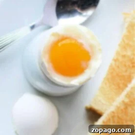 Air fryer soft-boiled egg in an egg cup, accompanied by toast slices and a spoon, all elegantly arranged on a white plate.