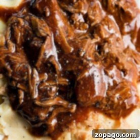 Tender rich turkey neck gravy over mashed potatoes on a white plate, accompanied by a fork.