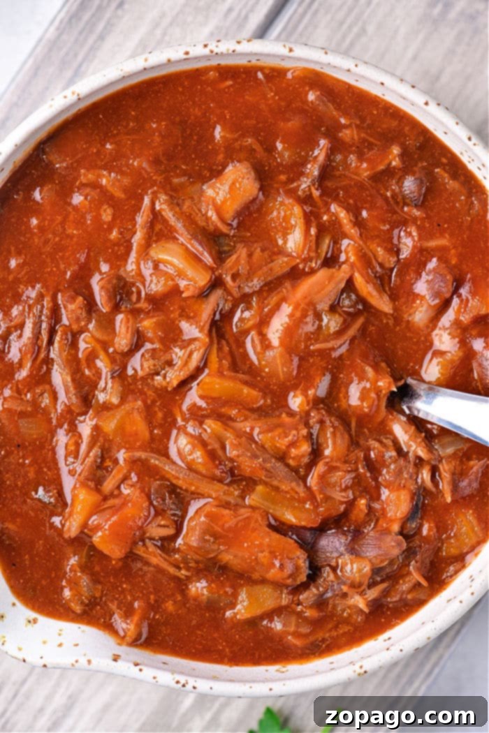 Slow-Simmered Turkey Neck Gravy 8 A bowl of rich gravy with shredded turkey neck meat and vegetables, served with a silver spoon, highlighting its hearty texture.