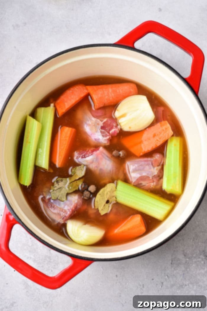 Tender Boiled Turkey Necks 3 Turkey necks simmering with aromatic vegetables in a pot of savory broth