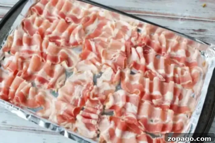 Perfect Oven Bacon on Foil 4 A baking tray lined with aluminum foil is covered with neatly arranged strips of raw bacon, ready to be cooked in the oven.